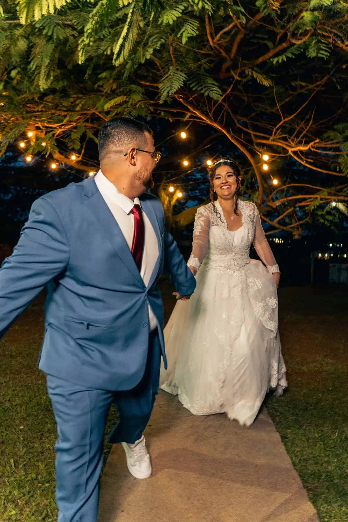Douglas e Ana caminhando de mãos dadas sob as luzes de varal à noite
