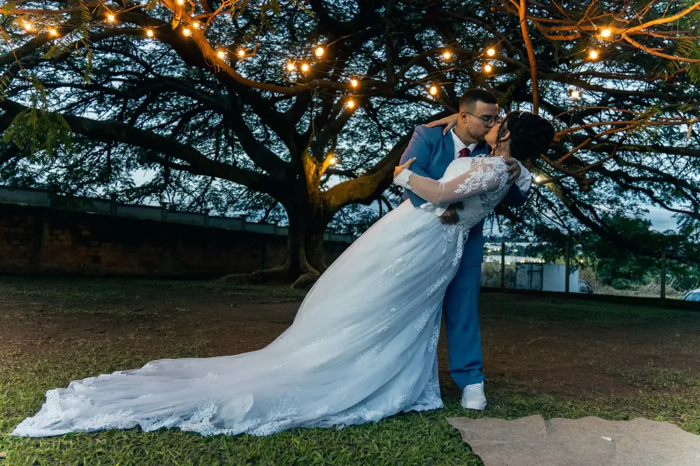 Douglas e Ana se beijando sob a árvore iluminada ao entardecer